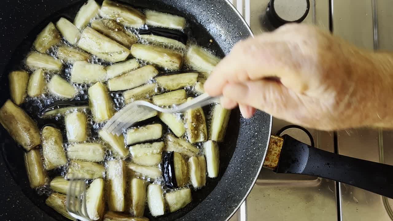 manos masculinas mezclando berenjenas fritas con tenedores en aceite vegetal