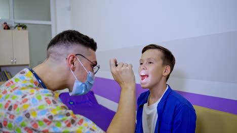a young male pediatrician examines the throat of a boy. checking throat of a sick little boy with a flashlight in the hospital.