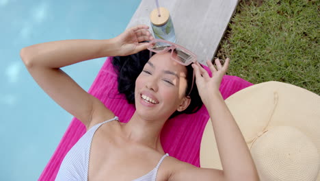 una joven biracial yace en un flotador de piscina rosa, sonriendo con los ojos cerrados