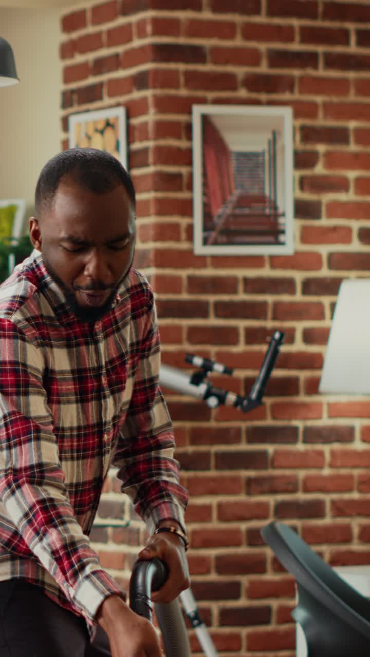 Vertical video: African american couple having fun spring cleaning with mop and vacuum cleaner