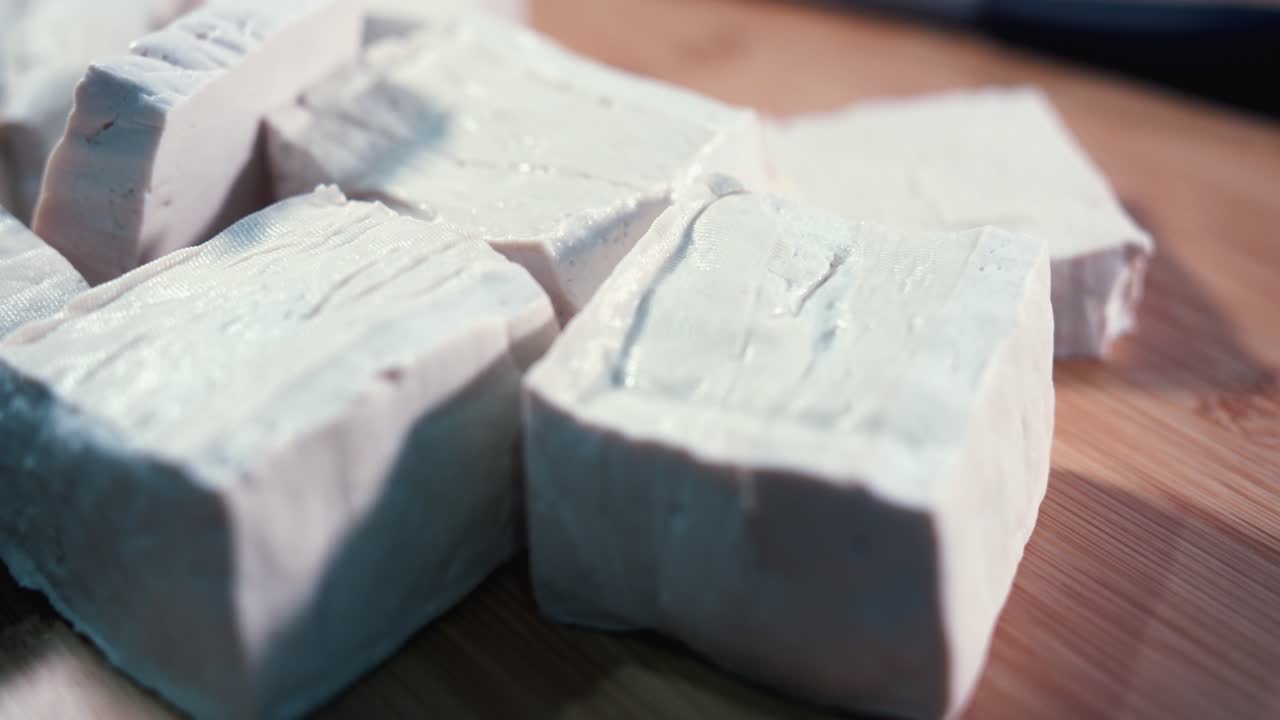 Gros plan en intérieur de gros dés de tofu tournant sur une surface en bois vers la droite.