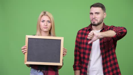young couple holding blackboard giving thumbs down together