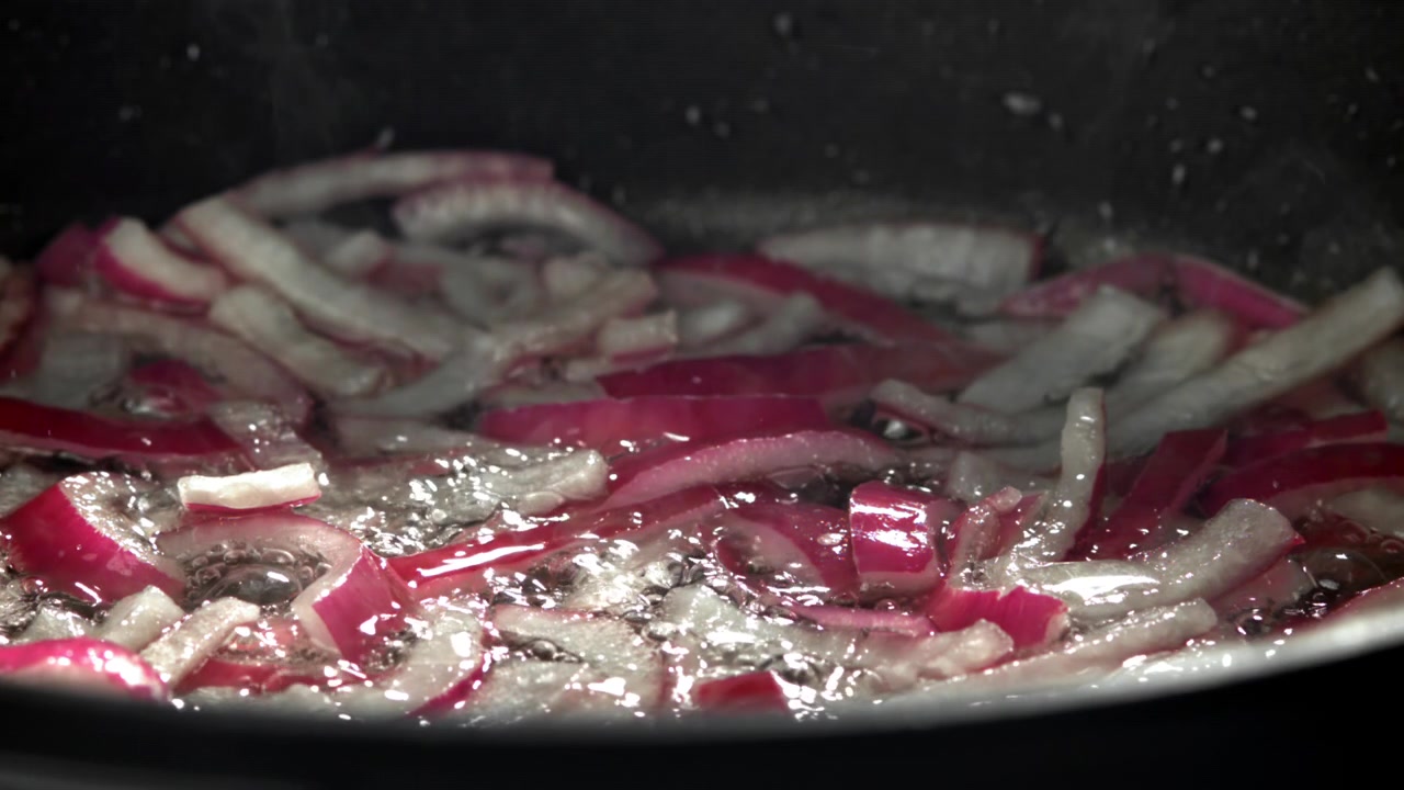 Primo piano di cipolle rosse affettate che friggono in olio caldo