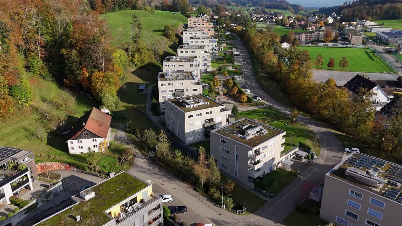 Residential buildings with green rooftops in a swiss town surrounded by autumn trees, aerial view