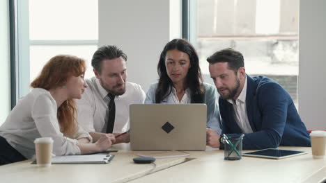 a young working team composed of two women and two men consulting the laptop together in a work meeting