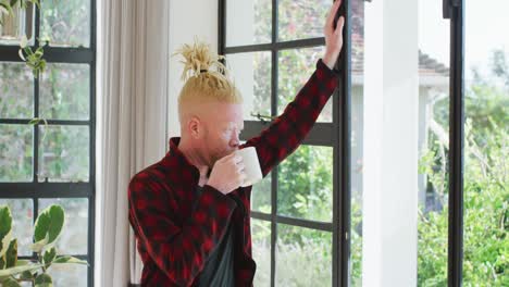 ein nachdenklicher albiner afroamerikanischer mann mit dreadlocks, der kaffee trinkt und ins fenster schaut