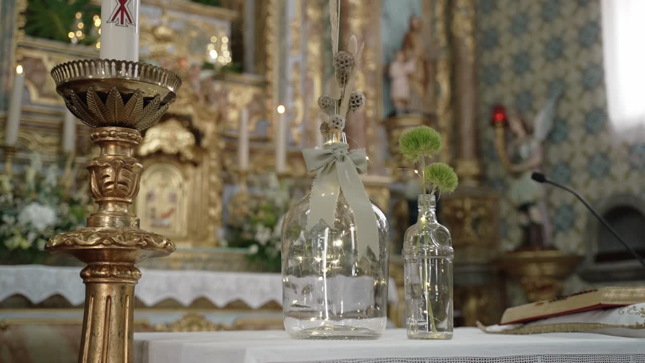 Close up of a decorated church altar featuring candles, glass vases, and floral elements