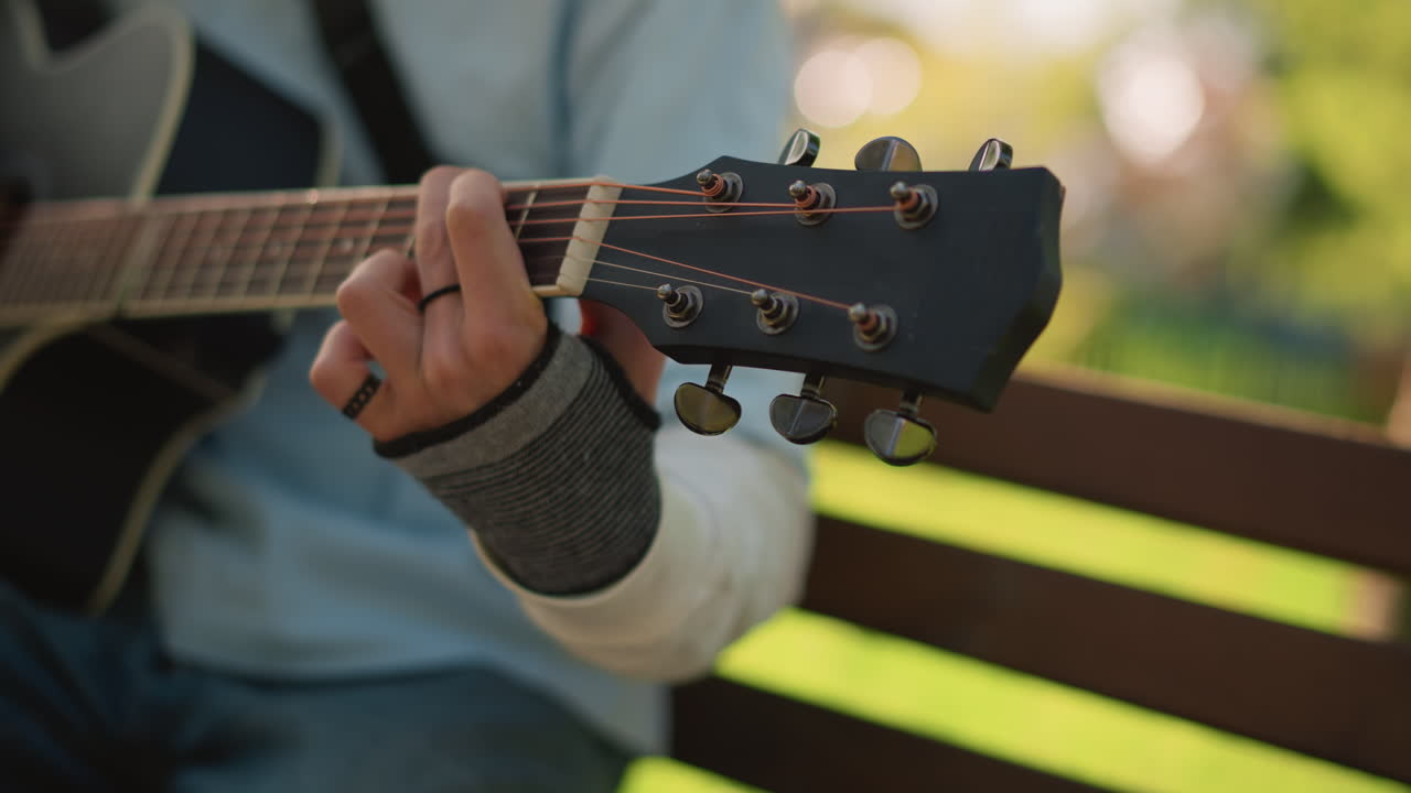 closeup left hand fretting acoustic guitar bench, soft sunlight and warm bokeh, songwriter practicing fingerstyle chords, intimate rehearsal with worn strings and focused technique