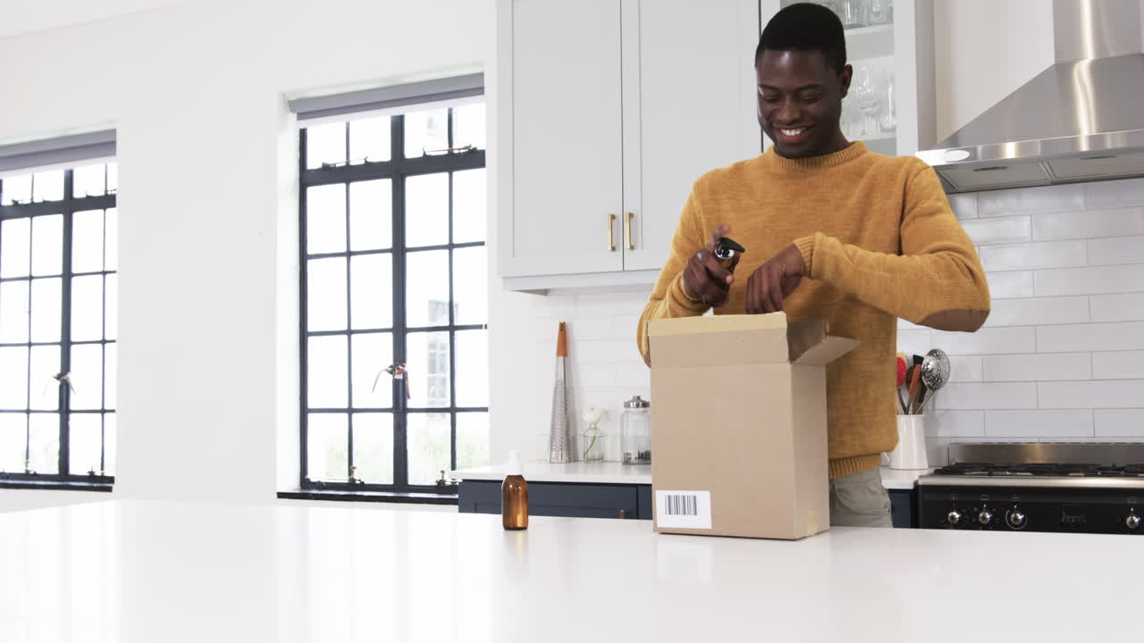 African American man unpacking gift box in kitchen, smiling with excitement, copy space