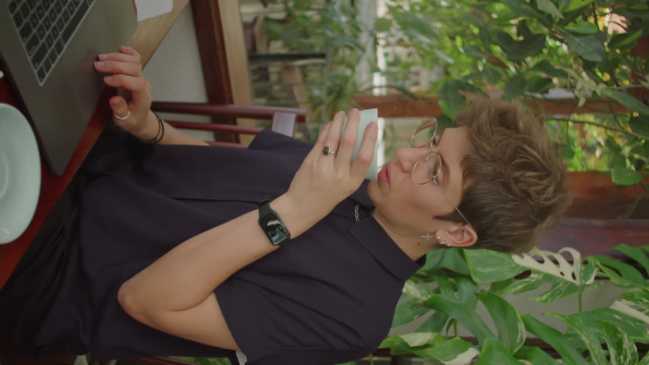 Woman Drinking Coffee and Working on Laptop in Outdoor Cafe