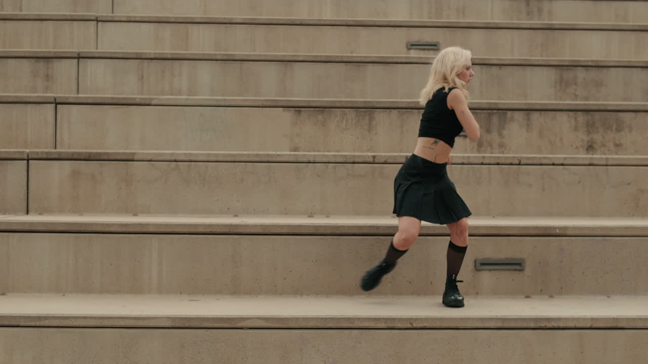 Giovane donna bionda che esegue danza contemporanea su scalini urbani