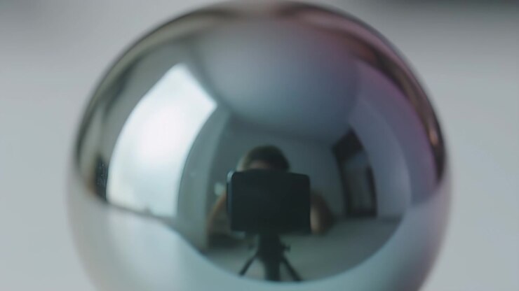 Riflesso di una macchina fotografica e di un fotografo in una sfera di metallo lucido