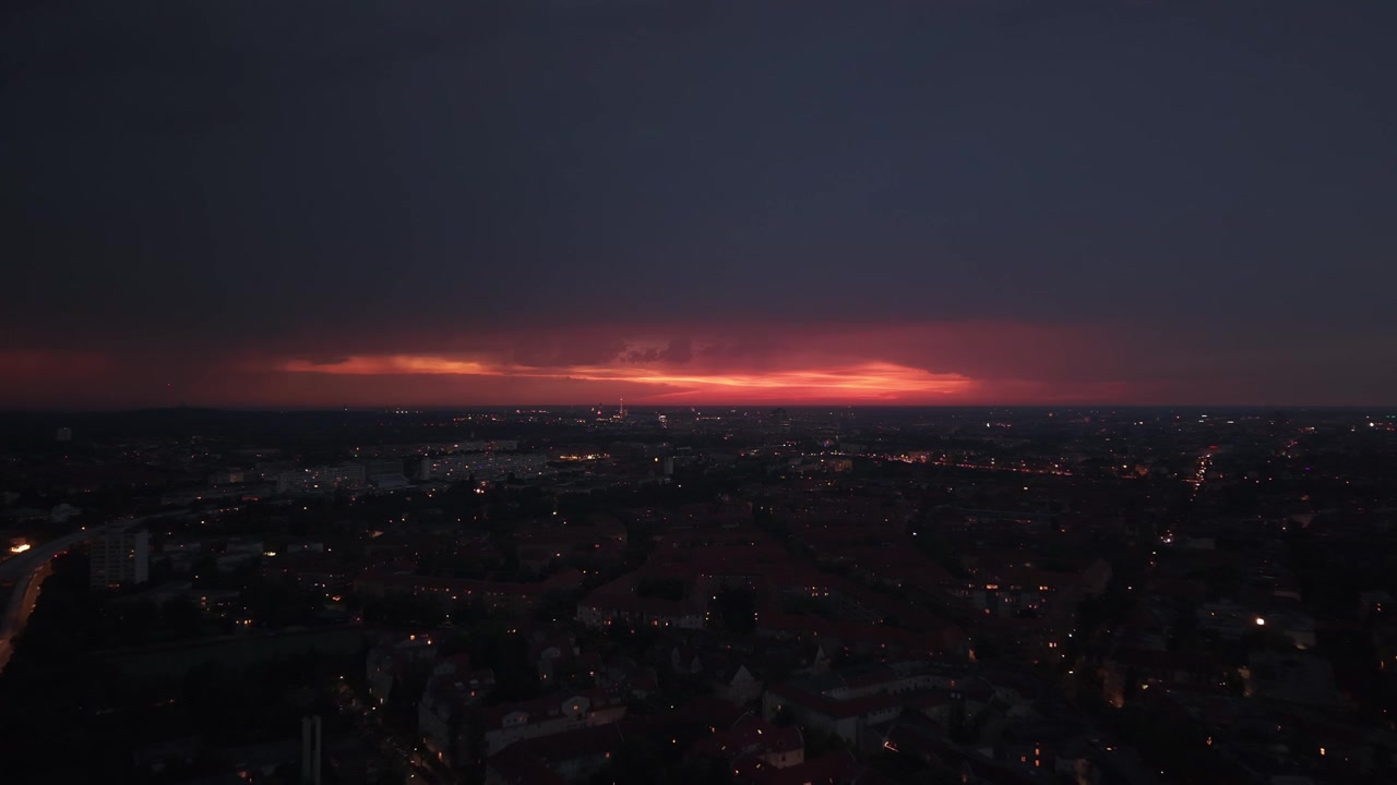 Tmavé mraky pokrývající panorama Berlína s pouličními lampami zářícími při západu slunce. Nejlepší letecký záběr, panorama z dronu letícího vpřed.