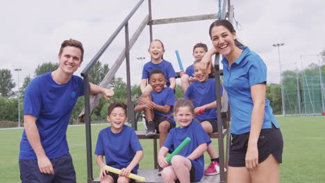 Retrato-De-Niños-Con-Entrenadores-Masculinos-Y-Femeninos-Preparándose-Para-La-Carrera-De-Relevos-En-El-Día-Del-Deporte