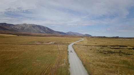 Vehículo-Que-Navega-Por-Un-Camino-Accidentado-Y-Sin-Pavimentar-Rodeado-De-Un-Terreno-árido-Y-Expansivo-Con-Montañas-Pintorescas,-Bañado-Por-El-Cálido-Resplandor-De-Un-Día-Soleado