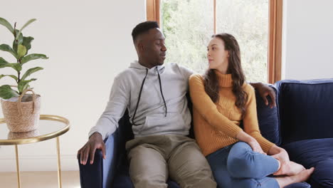 happy diverse couple sitting on sofa talking and smiling in home,copy space