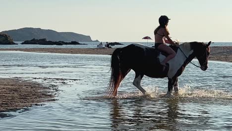 little girl wearing swimsuit enjoy sunset bareback riding horse in sea water in summer season in corsica, france