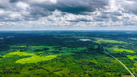 a breathtaking aerial timelapse captures dramatic clouds moving quickly across the sky above a long, winding road that cuts through the dense green forests of latvia