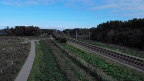 dutch train is driving away from the drone on a railway track true the dutch nature on a sunny blue sky day