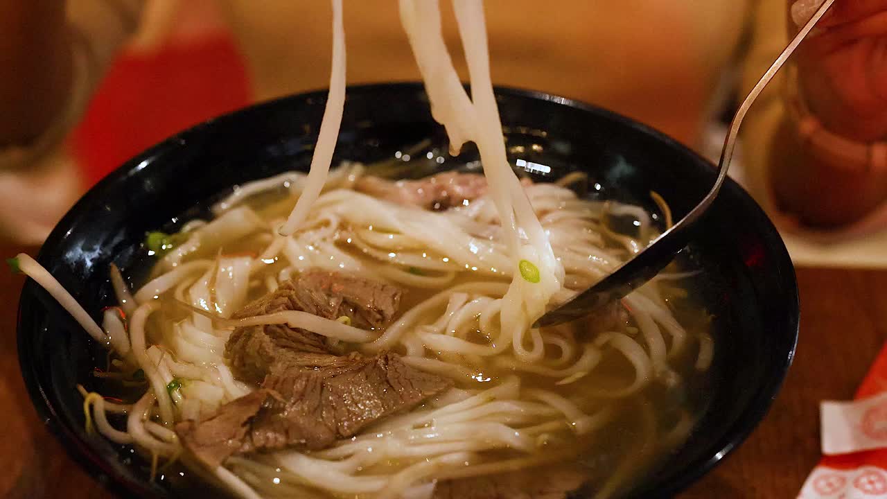 A person savors a bowl of Vietnamese pho with chopsticks and spoon in a cozy setting