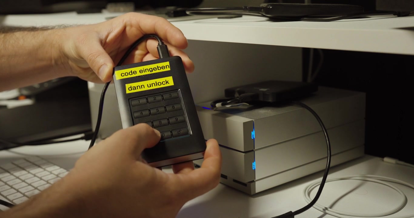 Person holding a password-protected external hard drive with keypad, demonstrating secure data storage and encryption.