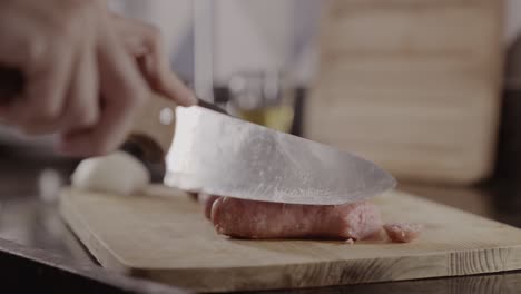 close-up of hands chopping raw meat with a knife on a cutting board