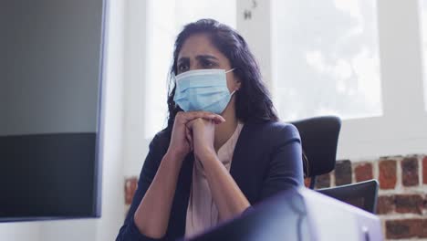 Woman-wearing-face-mask-sitting-on-her-desk-at-office