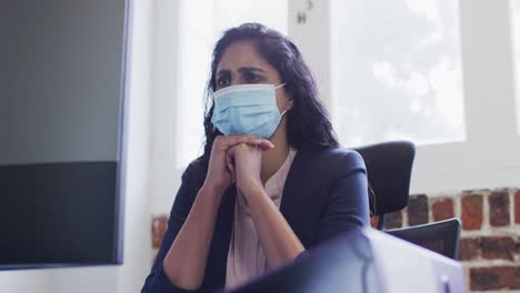 mujer con máscara facial sentada en su escritorio en la oficina