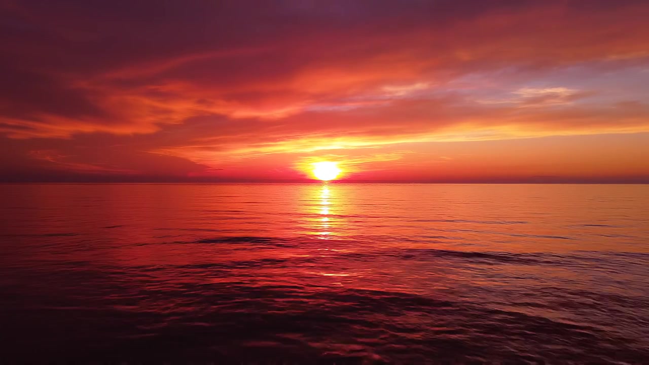 Vibrant orange sunset over calm ocean waters with dramatic sky