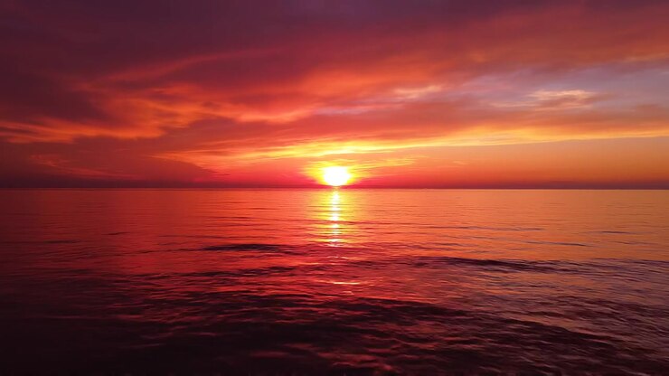 Vibrant orange sunset over calm ocean waters with dramatic sky