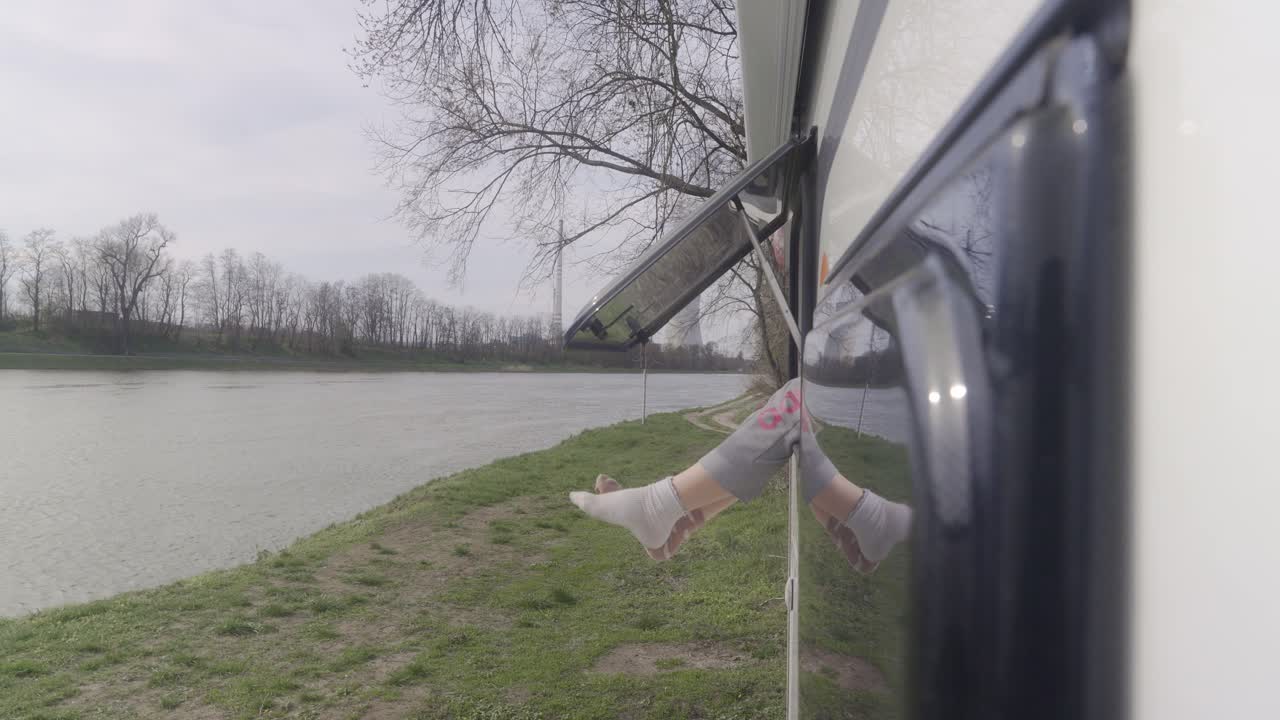 울창한 초록색으로 둘러싸인 강의 조용한 전망을 즐기며 차량 창문 밖으로 기울어지는 사람