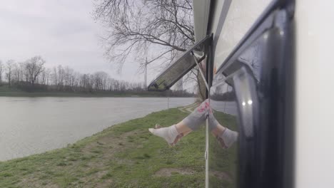 persona inclinada por la ventana de un vehículo, disfrutando de la vista serena de un río rodeado de exuberante vegetación
