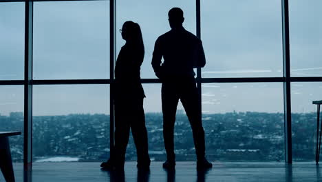 male silhouette stands his back to camera drinking coffee. female silhouette walks to and fro speaking on the phone.
