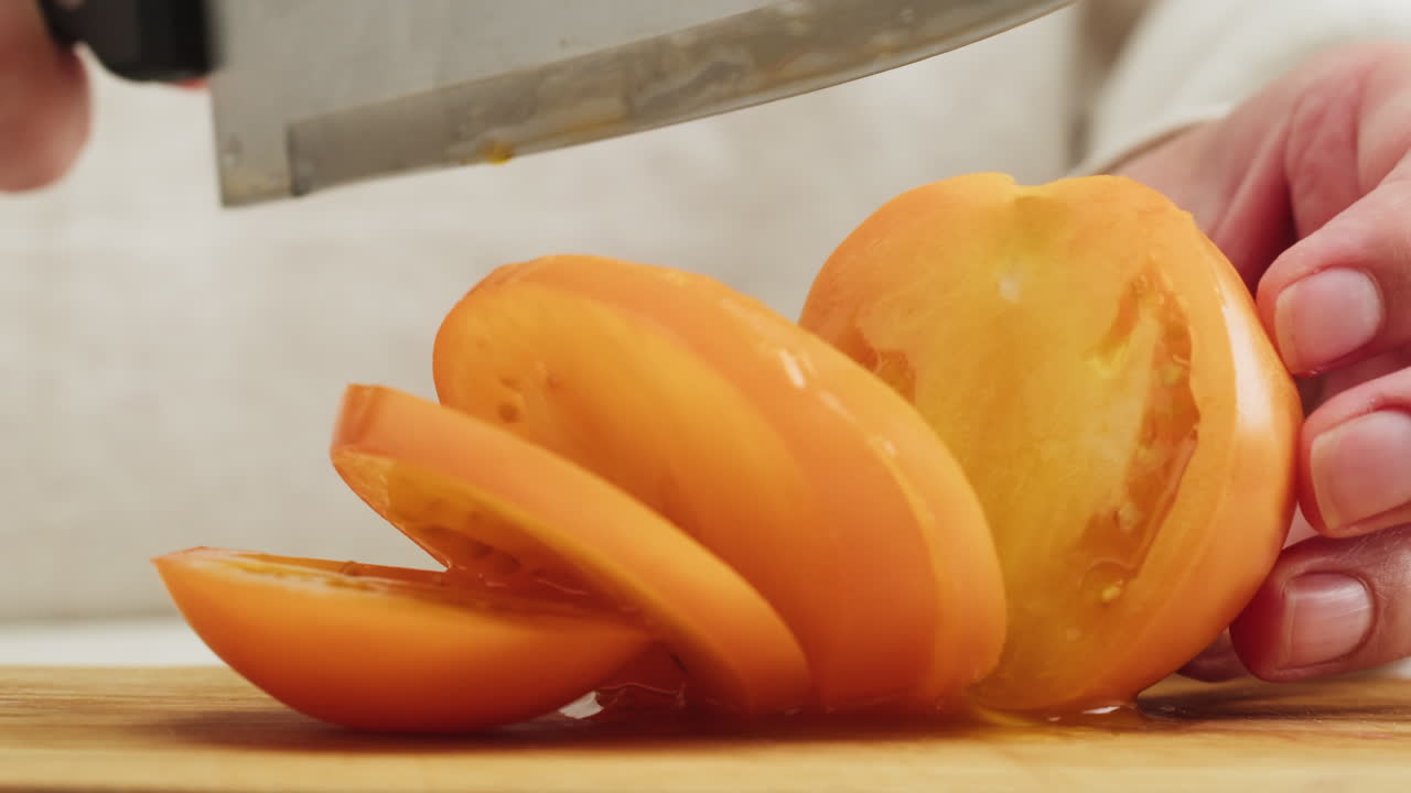 Close Up of Hands Slicing a Fresh Yellow Tomato on a Cutting Board