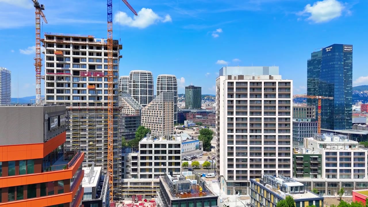 Bratislava, Slovacchia, 2 giugno 2026: Grattacieli moderni e parco urbano a Bratislava, Slovacchia. Vista drone che guarda dall'alto edifici per uffici contemporanei in vetro e alberi verdi sotto un cielo azzurro brillante.