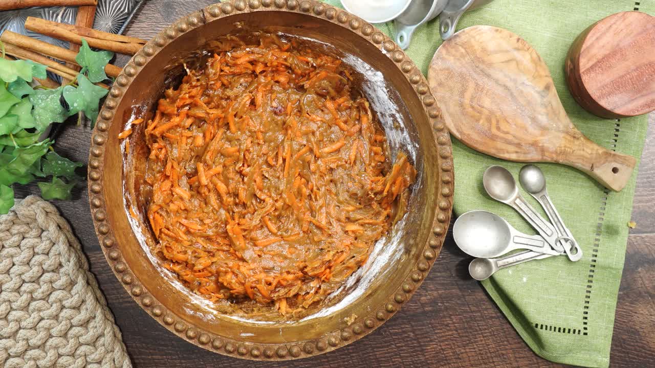 Baking a carrot cake loaf with cream cheese icing and topped with roasted salted pecans. Making a Autumn dessert with carrots, flour, sugar, nuts and frosting. Mixing the carrots into the batter.