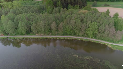 Family-walking-around-the-lake-along-a-path-on-a-sunny-summer-day,-some-riding-a-bike