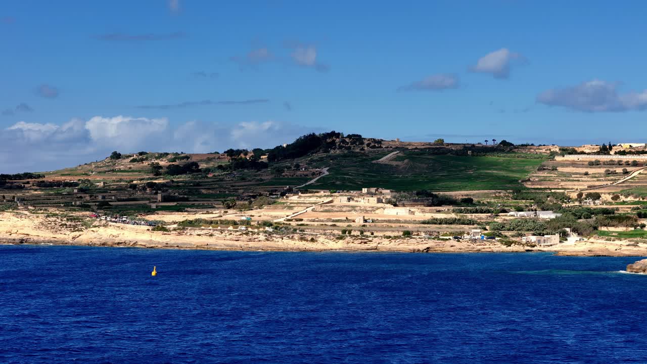 Vista panorámica de gran angular de la escarpada costa maltesa bajo un brillante sol de verano, con las emblemáticas colinas escalonadas de Gozo, los dorados acantilados de piedra caliza y las profundas aguas azules del mar Mediterráneo