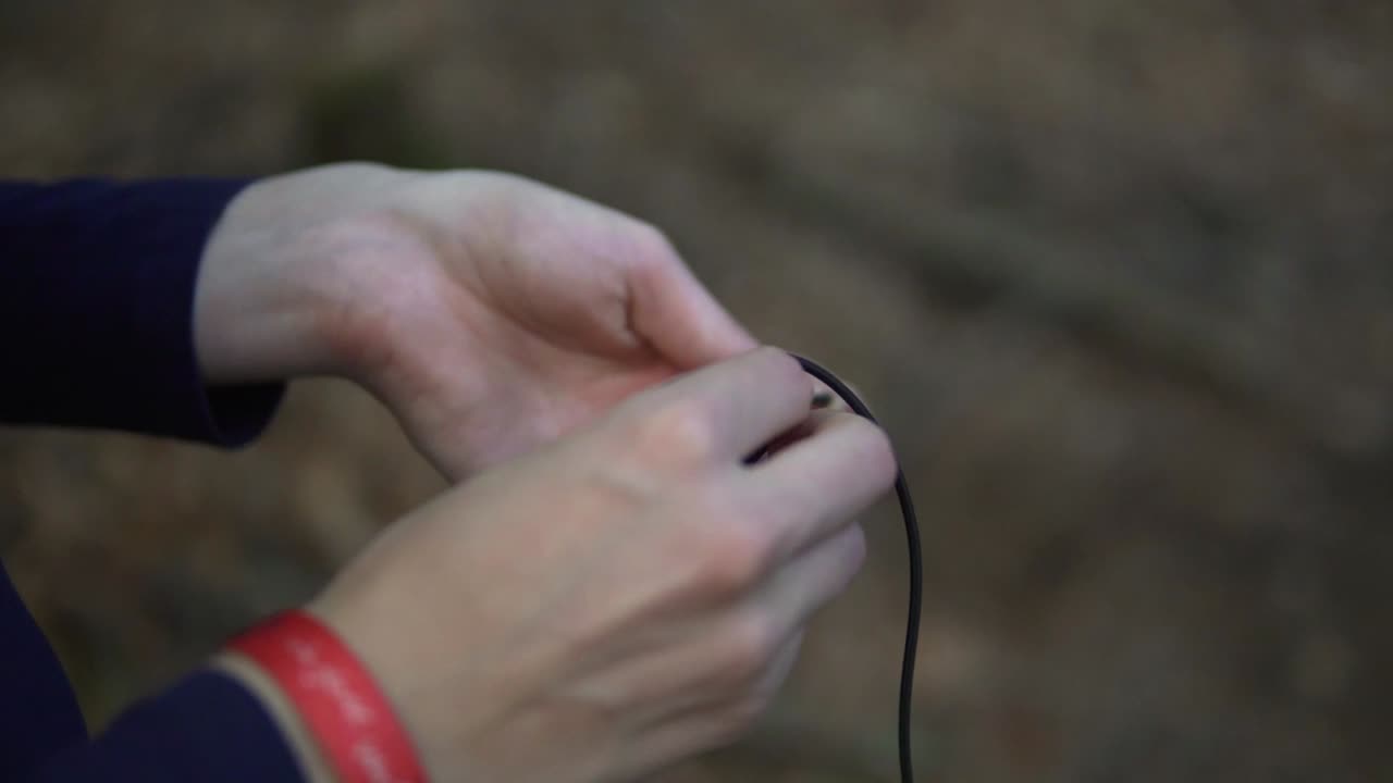 In a close-up video taken in a forest in Germany, a man is seen using his hands to tie a knot or knoten in a black rope