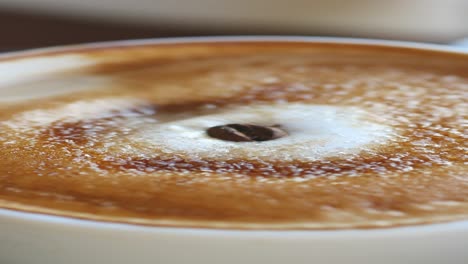 close up of a cup of coffee with a sprinkle of sugar and a coffee bean on top.