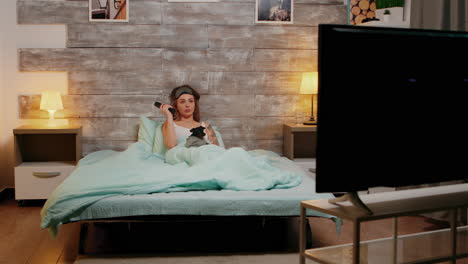 mujer relajada en pijama viendo la televisión acostada en la cama