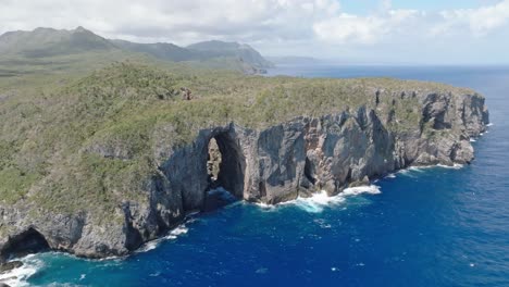 aerial establishing shot of beautiful cabo cabron nationalpark with natural arches, steep cliffs and crashing waves of blue caribbean sea during cloudy day - panorama view