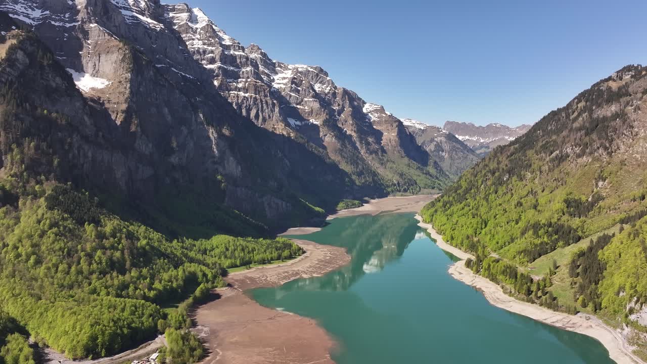Aerial view of Klöntalersee in Klöntal Valley, Glarus, Switzerland, surrounded by the steep slopes of Vorderglärnisch mountain and lush spring greenery reflecting in the calm turquoise lake