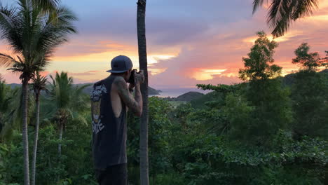 male freelance photographer taking sunset photo through jungle forest from villa in lombok