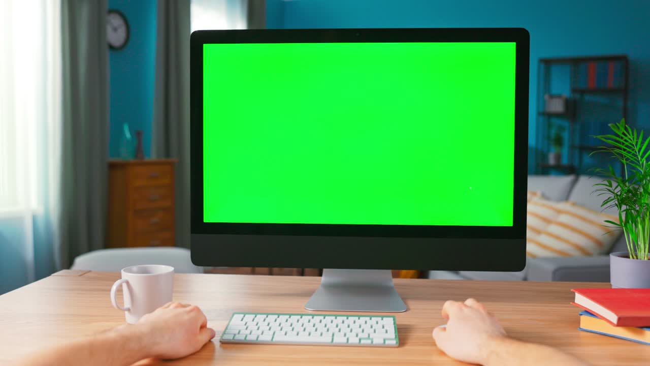 남자 손의 클로즈업은 컴퓨터 마우스를 사용합니다. 편안한 홈 오피스의 책상 위에 서있는 모형 녹색 화면 디스플레이를 가진 현대 개인 컴퓨터에 확대합니다.