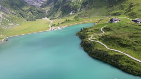 fpv view of an alpine clear water lake in the swiss alps, sinuous stone path for bikers and families, mountains behind, obwalden, engelberg