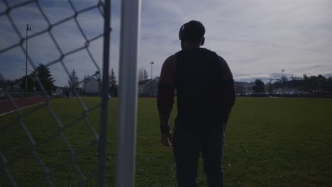 Male-Walking-Near-Metal-Fence-With-Headphones-On---Strong-Athletic-Muscular-Black-Man-Fitness-Outdoor-Training-Preparation-In-4K