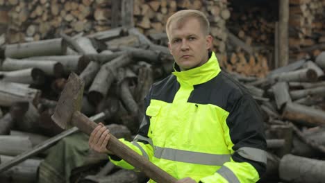 Lumberjack-in-reflective-jacket.-Man-woodcutter-with-big-axe.-Sawn-logs,-firewood-background