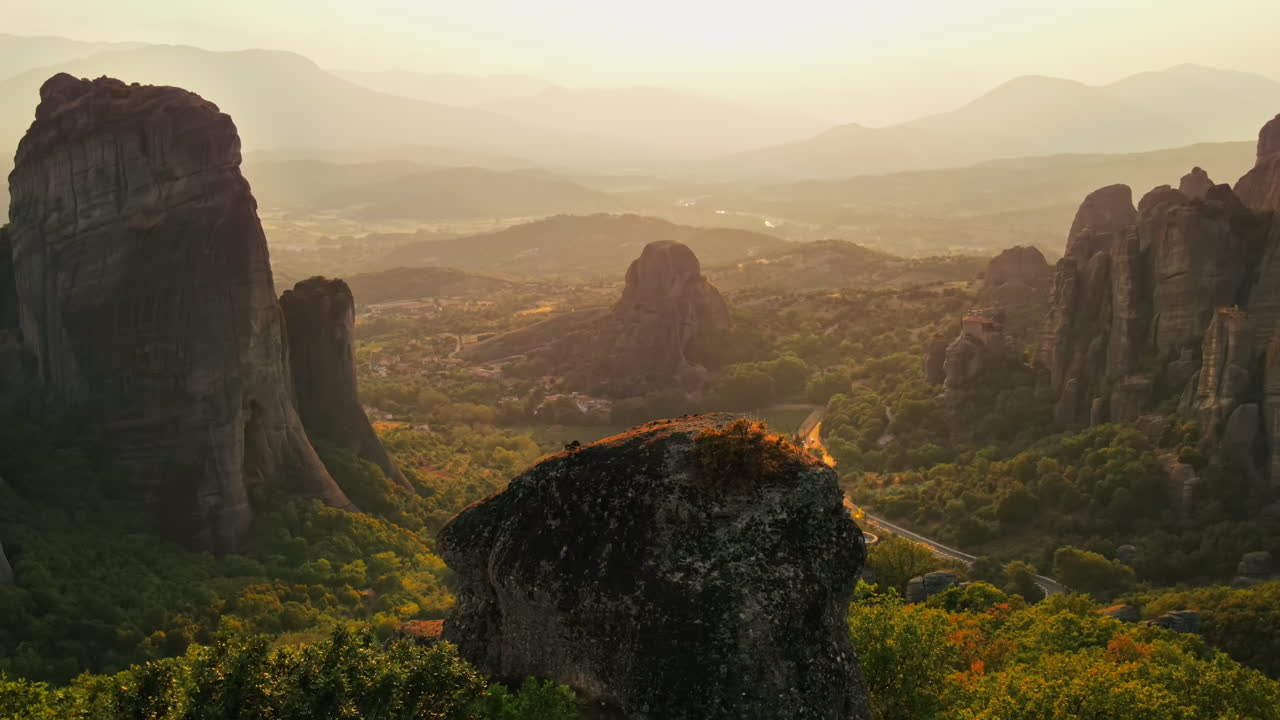 Aerial drone view of the Meteora in Greece at sunset. Rock formations with Orthodox monasteries. A lot of greenery, sacred place, road with cars