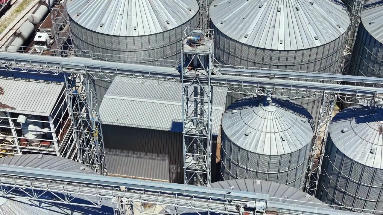 Industrial site with metal silos and machinery in operation near a railway track in broad daylight